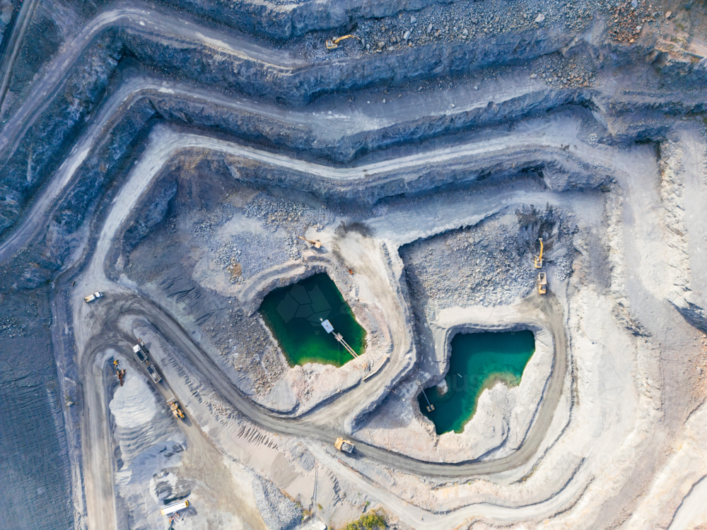 Aerial view looking down into a tiered quarry pit with machinery and water ponds - Australian Stock Image