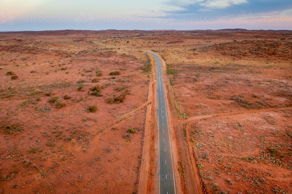 Aerial view of a bitumen road running through and arid outback landscape at twilight - Australian Stock Image