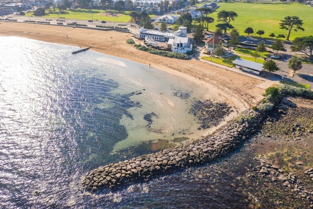 Aerial view of a breakwater shielding a narrow beach with surrounding parkland - Australian Stock Image