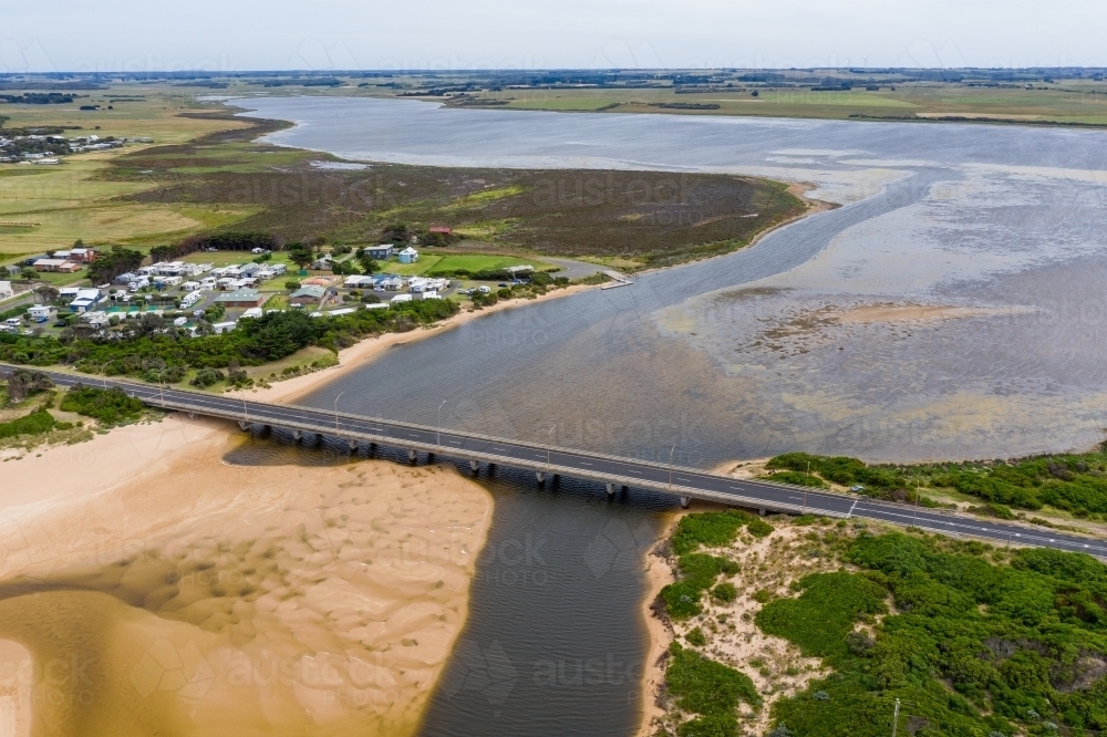 Aerial view of a bridge crossing a river flowing out to sea over a sandy beach - Australian Stock Image
