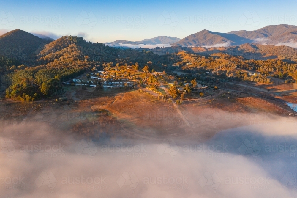 Aerial view of a caravan park on the shores of a mountain lake covered in fog - Australian Stock Image