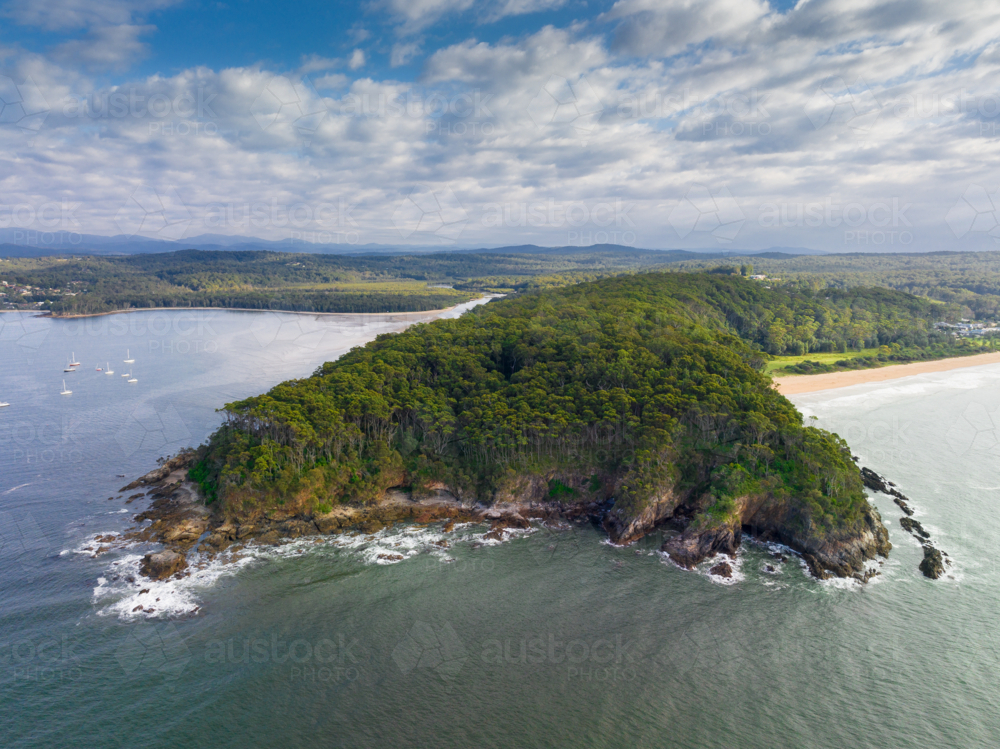 Aerial view of a coastal headland covered in dense vegetation and surrounded by a rocky shoreline - Australian Stock Image