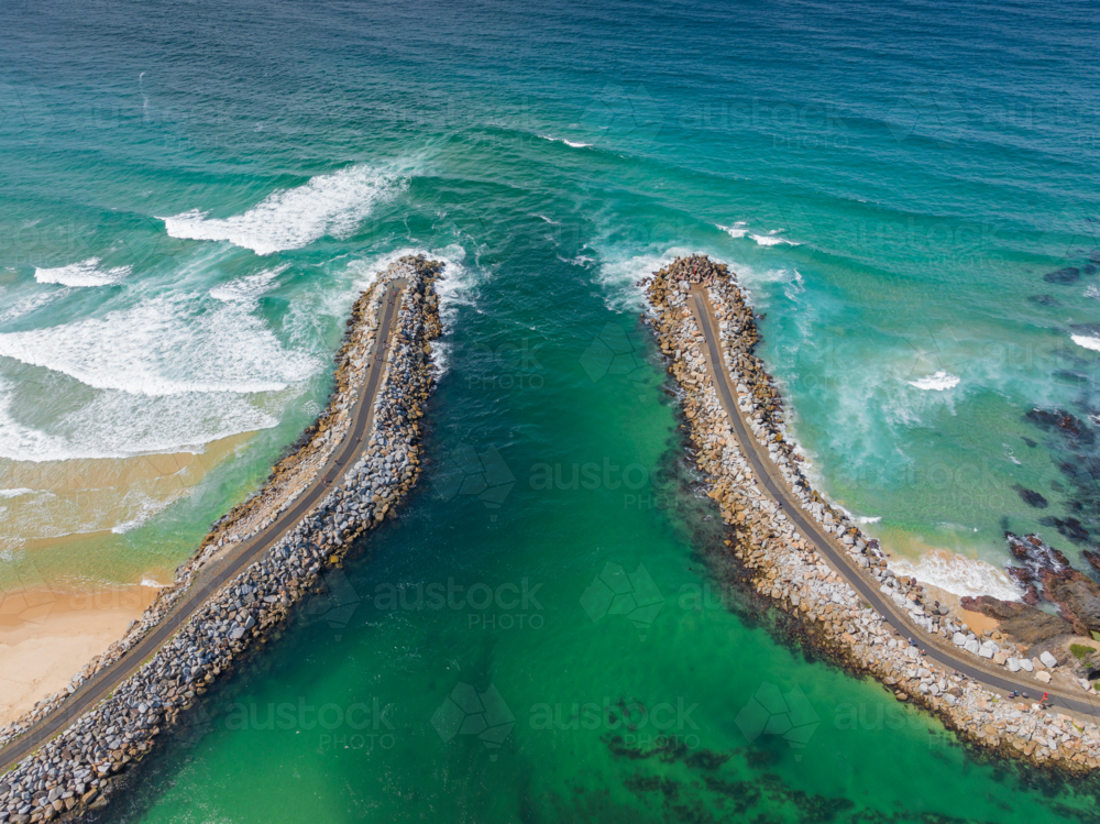 Aerial view of a coastal inlet flowing out to sea between two rocky breakwaters - Australian Stock Image