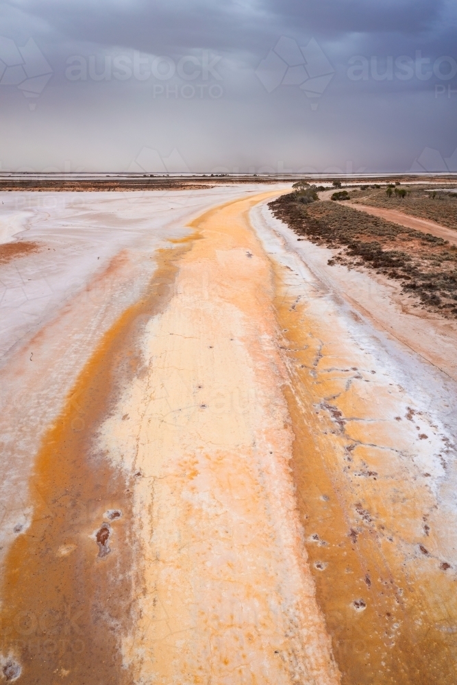 Aerial view of a colourful dried salt lake under dark dust laden sky - Australian Stock Image