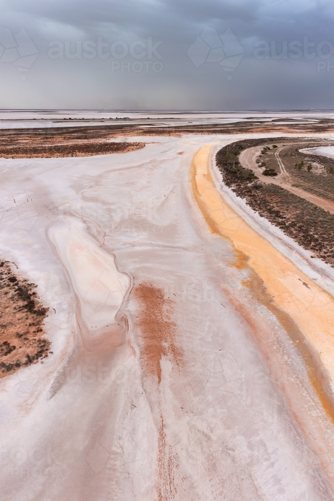 Aerial view of a colourful dried salt lake under dark dust laden sky - Australian Stock Image