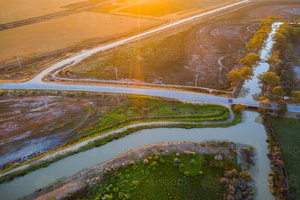 Aerial view of a country road crossing an irrigation channel at sunset - Australian Stock Image