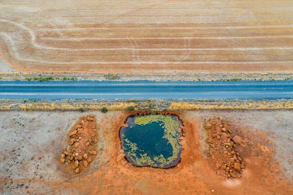 Aerial view of a country road next to a dam on dried farmland. - Australian Stock Image