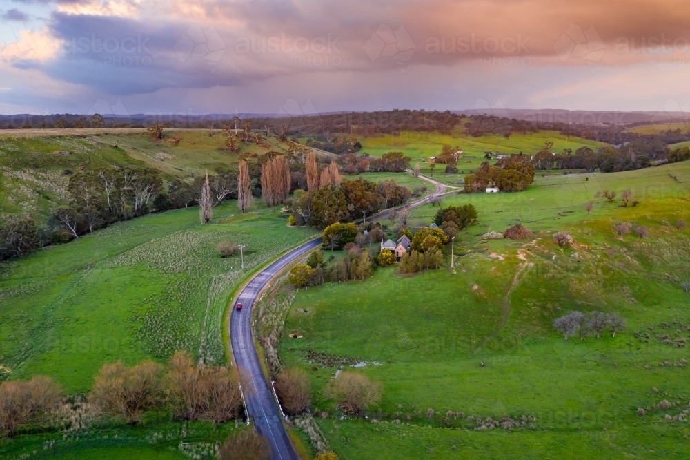 Aerial view of a country road running through green rural countryside under a stormy sky - Australian Stock Image