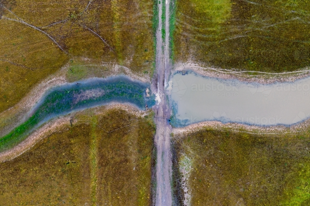 Aerial view of a dirt track crossing a drying river - Australian Stock Image