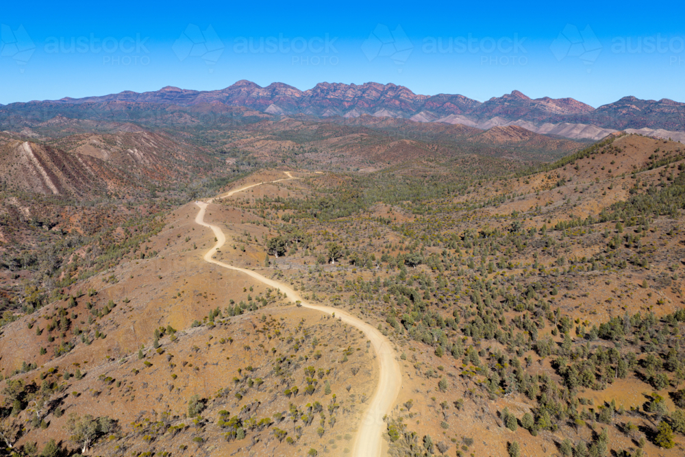 Aerial view of a dirt track curving through an arid valley toward mountains - Australian Stock Image
