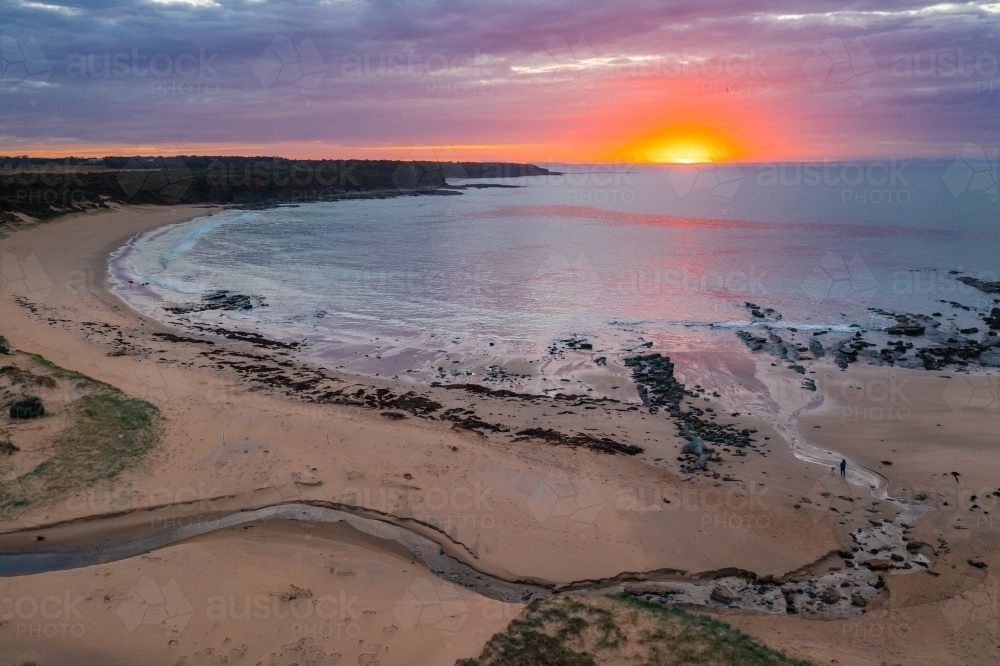 Aerial view of a dramatic sunrise over a deserted beach with creek flowing out to sea - Australian Stock Image