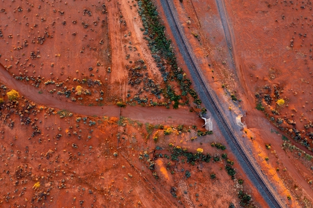 Aerial view of a dry creek bed running under a raised railway track through a barren orange outback - Australian Stock Image