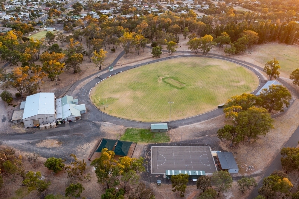 Aerial view of a dry sports oval and buildings surrounded by gum trees - Australian Stock Image