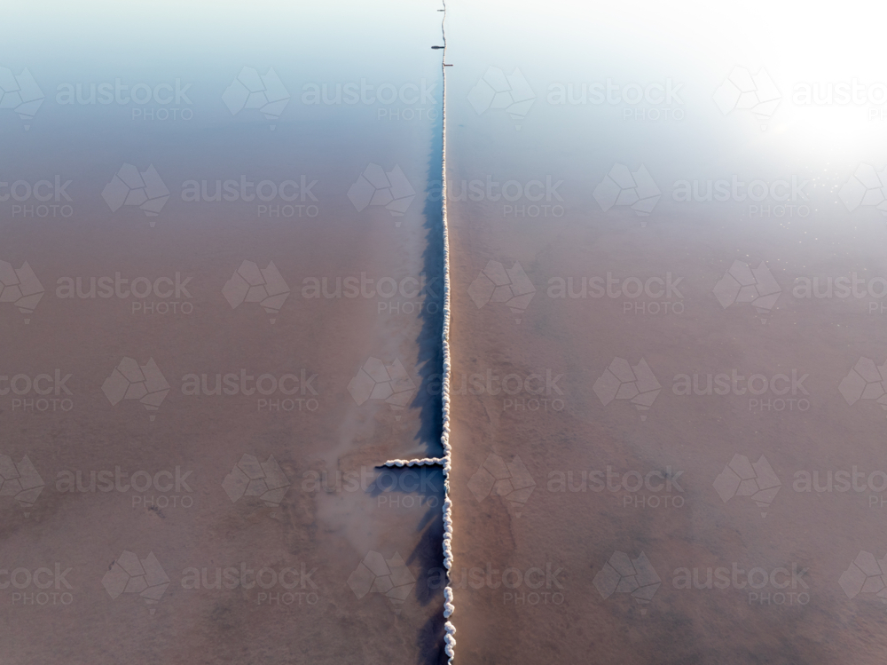 Aerial view of a fence running vertically through a pink salt lake - Australian Stock Image