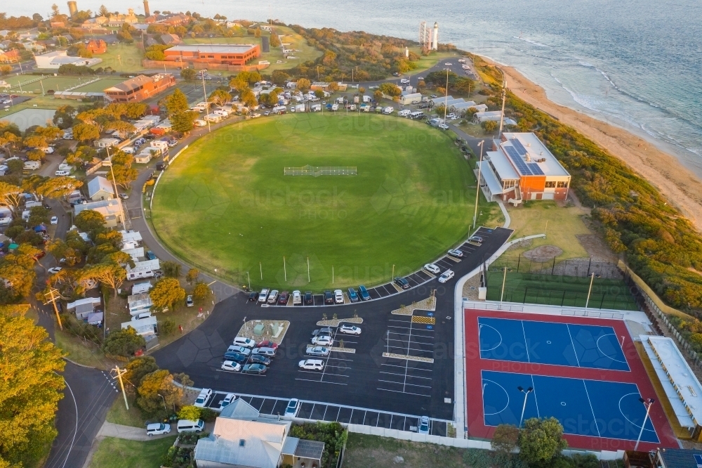Aerial view of a football oval and netball courts in a caravan park beside the ocean - Australian Stock Image