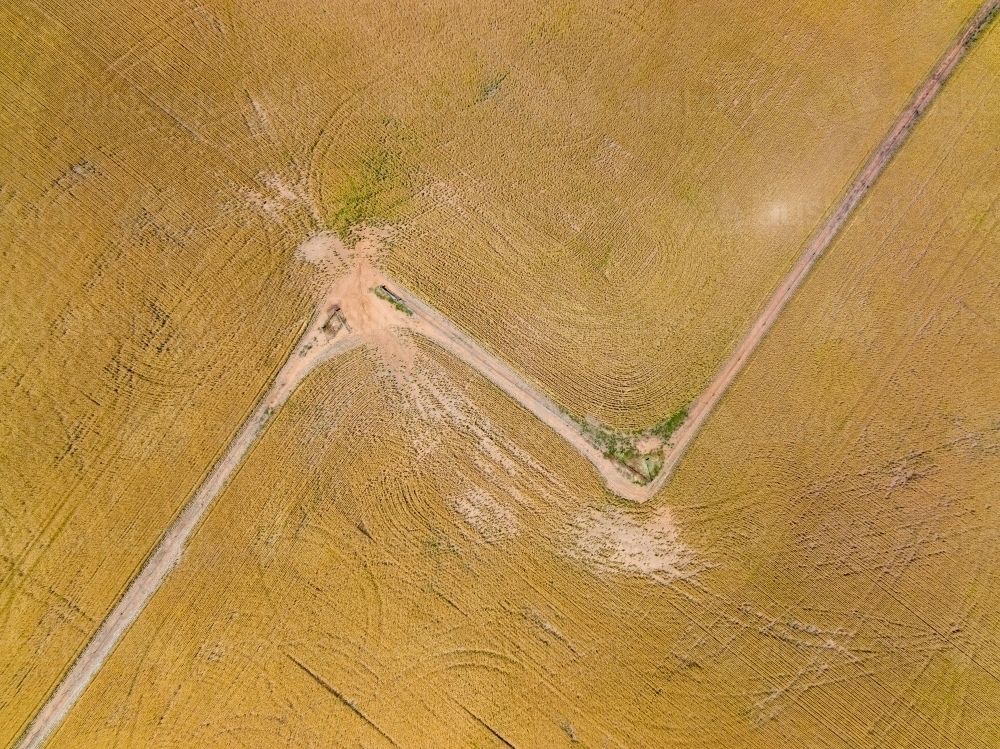 Aerial view of a gateway on the corner of a fence line between two dry paddocks with wheel tracks - Australian Stock Image