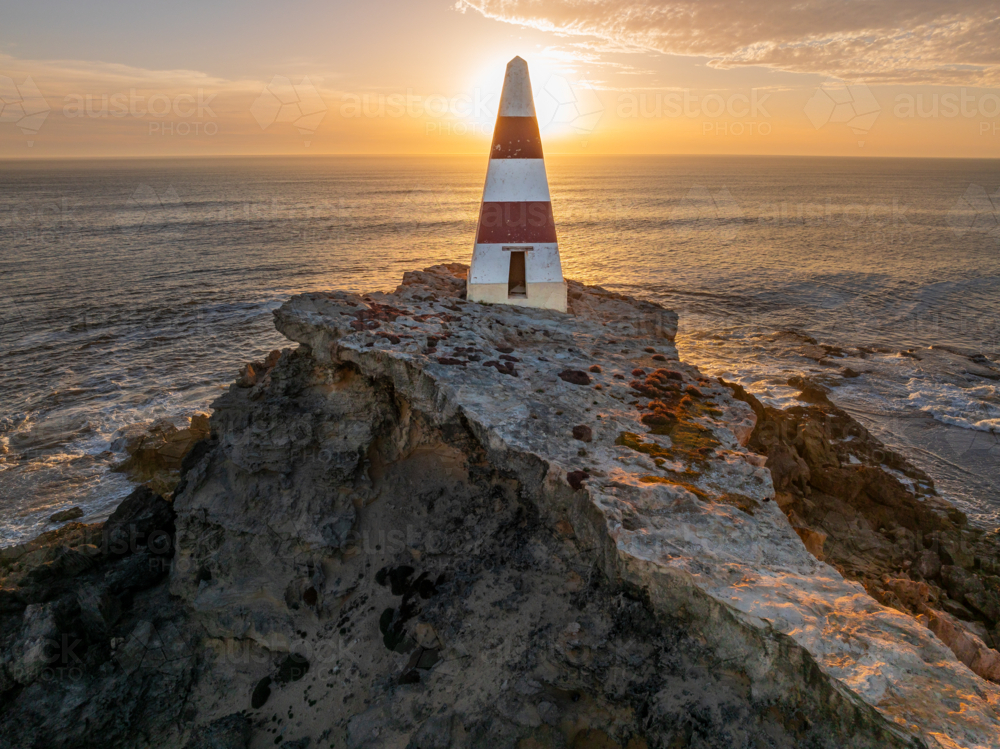 Aerial view of a golden sunset behind a obelisk monument on a rocky coastal cliff top - Australian Stock Image