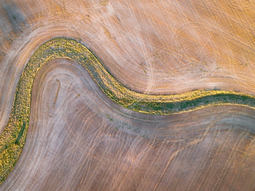 Image of Aerial view of a green creek bed winding through a ploughed ...