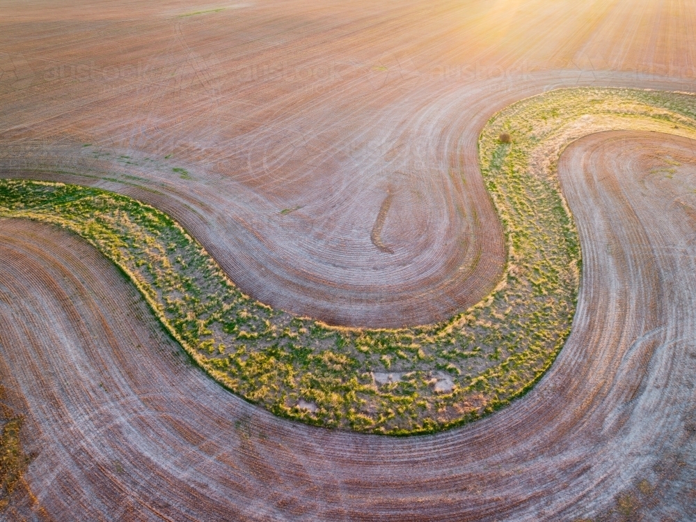 Image of Aerial view of a green creek bed winding through a ploughed ...