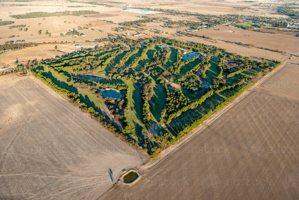Aerial view of a green golf course surrounded by dry farmland on the edge of a rural town - Australian Stock Image