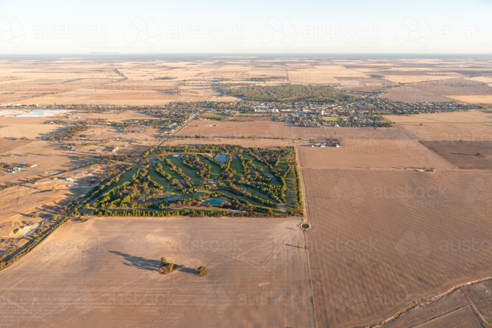 Aerial view of a green golf course surrounded by dry farmland on the edge of a rural town - Australian Stock Image