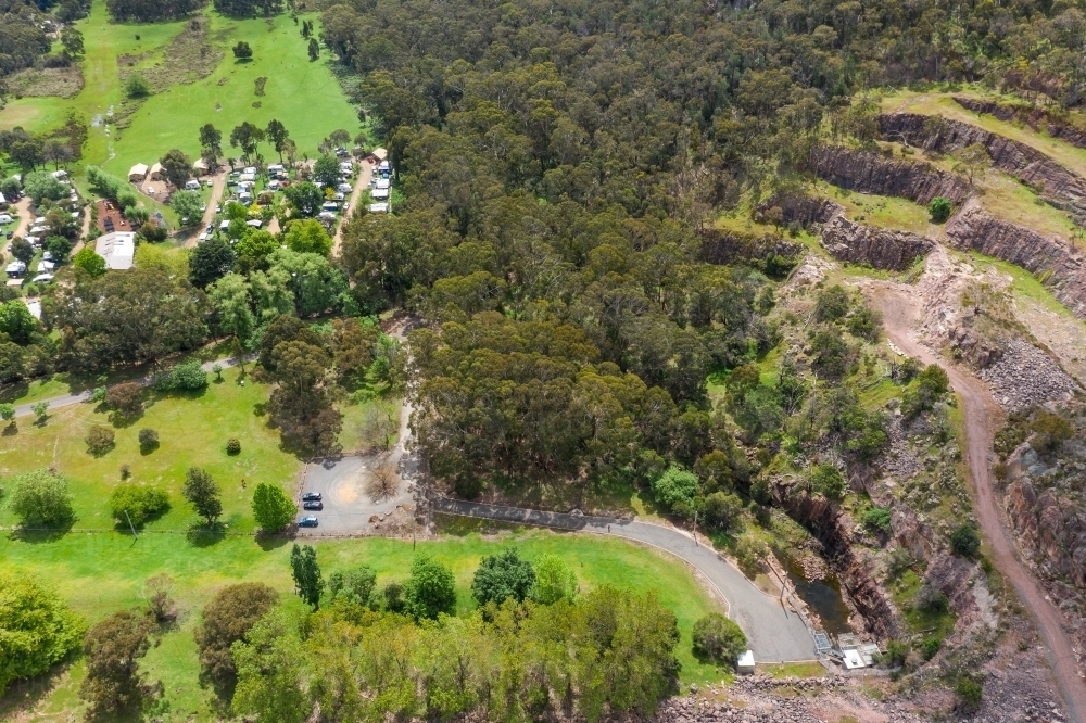 Aerial view of a green valley with a caravan park, forest and rocky terraces - Australian Stock Image