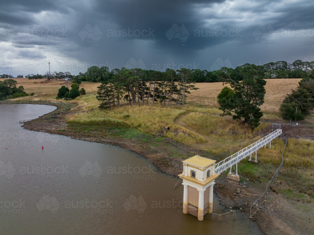 Aerial view of a heavy rain falling over a water tower along the shoreline of a rural reservoir - Australian Stock Image