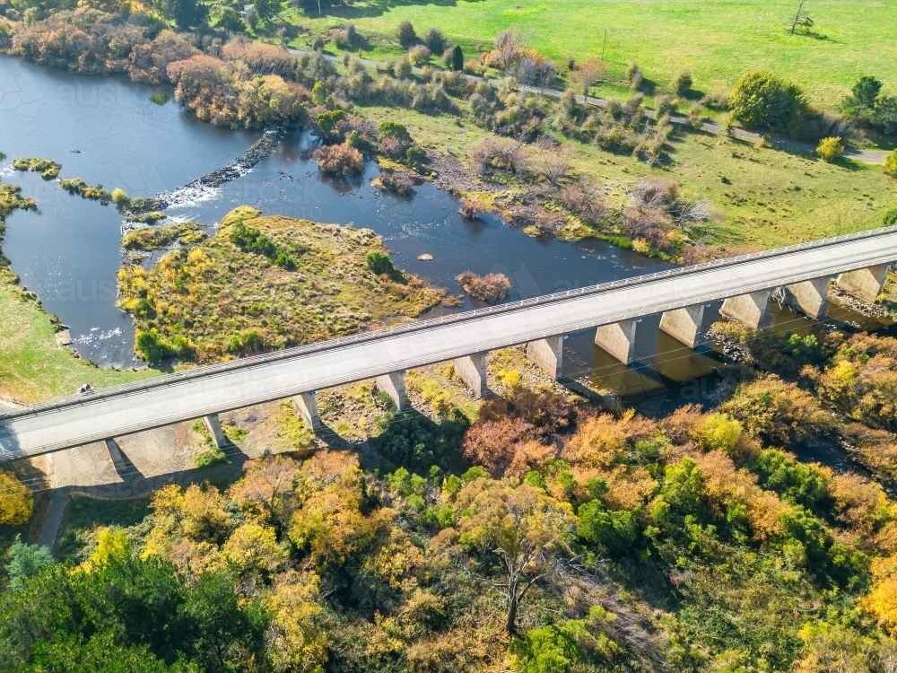 Aerial view of a high bridge over a river with autumn trees on the riverbanks - Australian Stock Image