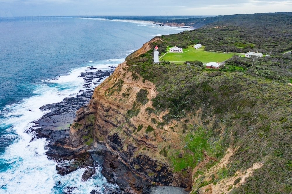 Aerial view of a lighthouse perched on a clifftop above a rugged coastline - Australian Stock Image