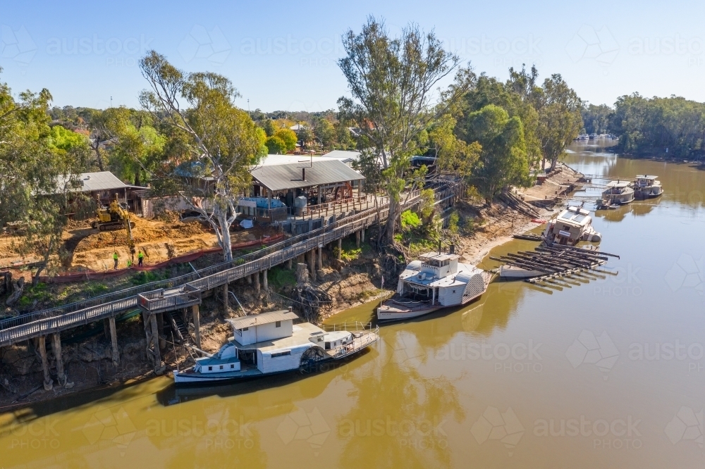 Aerial view of a line of paddle steamers anchored next to a high timber wharf on a river bank - Australian Stock Image