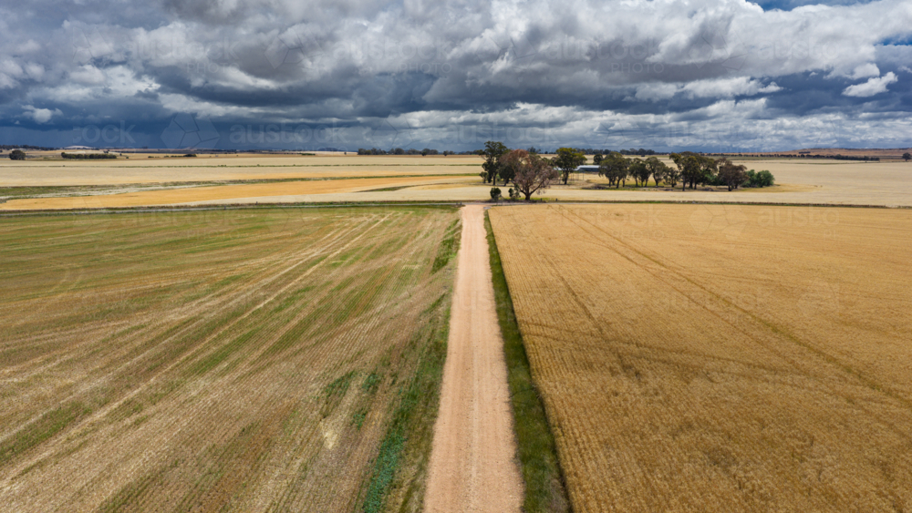 Aerial view of a long straight dirt road through farmland under dark storm clouds - Australian Stock Image