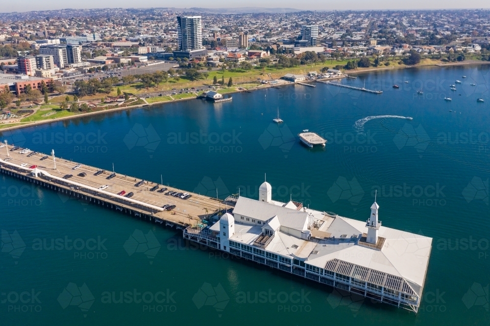 Aerial view of a long straight jetty with buildings on the end and a coastal city in the background - Australian Stock Image
