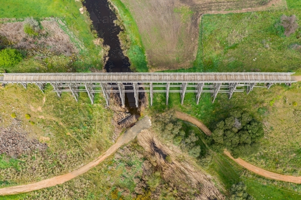 Image of Aerial view of a long wooden trestle bridge across a green