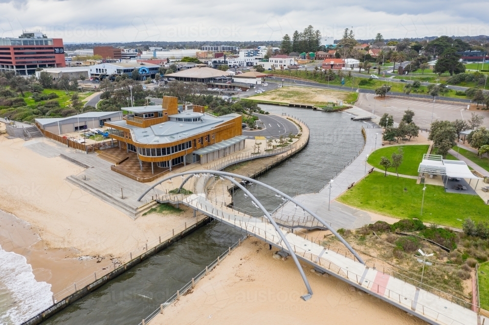 Aerial view of a modern arched walking bridge over a marina channel flowing out to sea. - Australian Stock Image