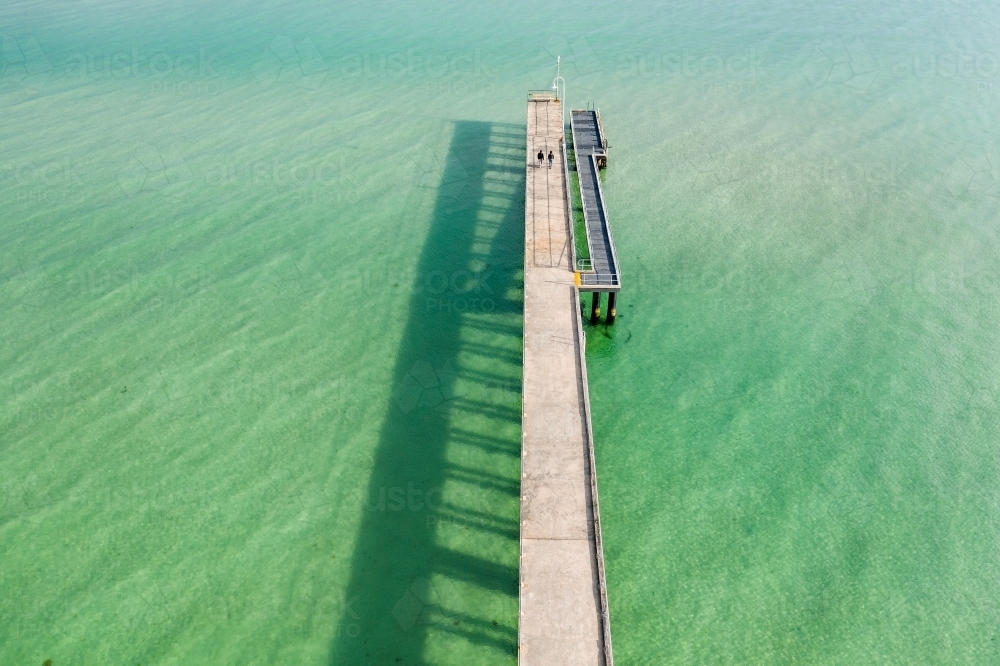 Aerial view of a narrow jetty and its shadow over  calm water - Australian Stock Image