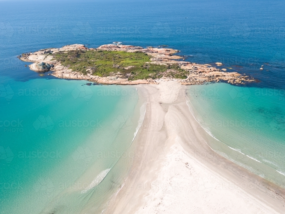 Aerial view of a narrow sandy beach leading out to a rocky island - Australian Stock Image