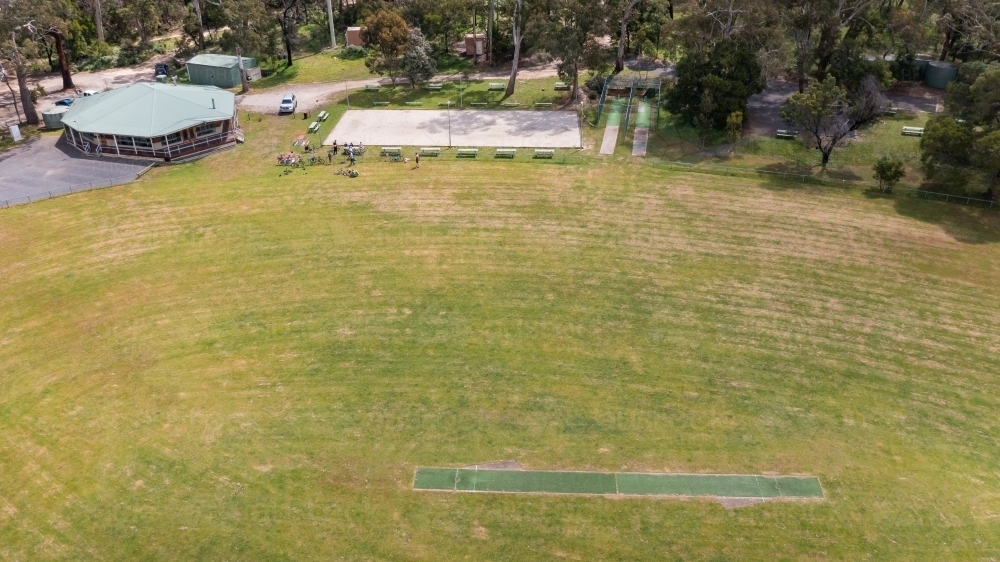 Aerial view of a people gathered at a grassy oval with a cricket pitch and clubrooms - Australian Stock Image