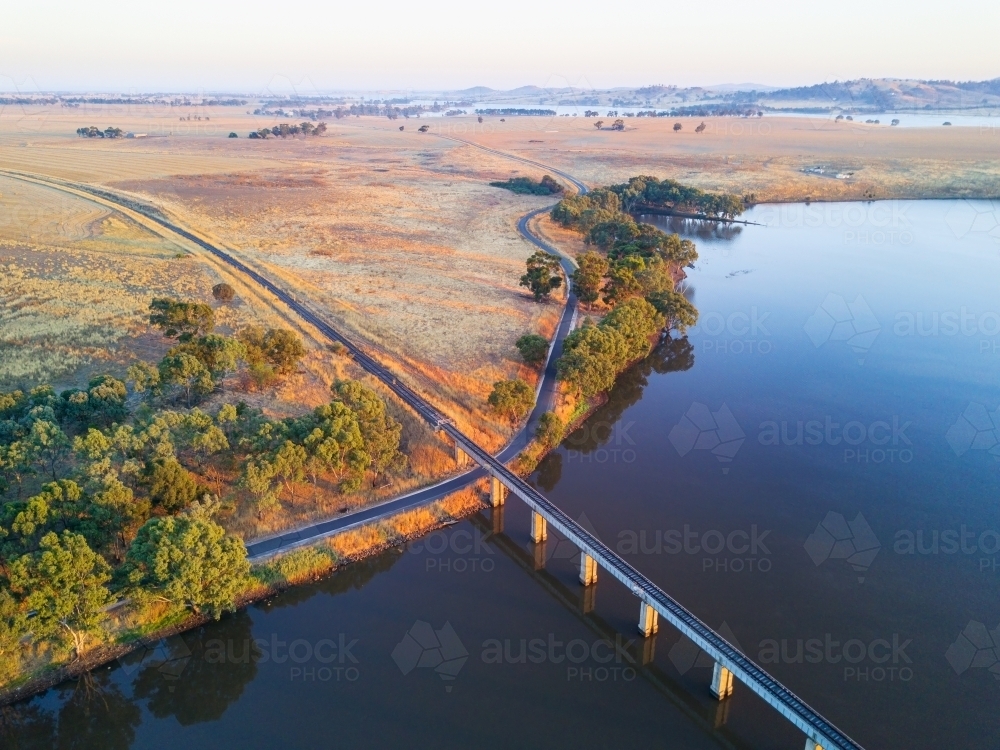 Aerial view of a railway bridge crossing a lake in early morning sunshine - Australian Stock Image