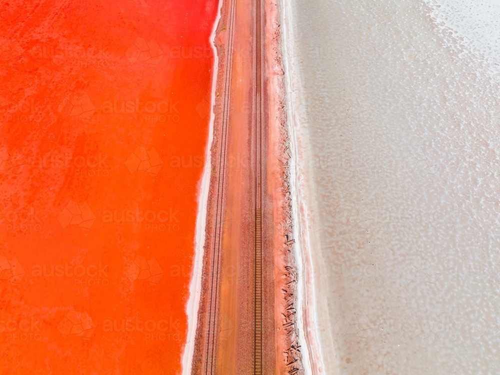 Aerial view of a railway line running across a salt lake with one side vivid red in colour - Australian Stock Image