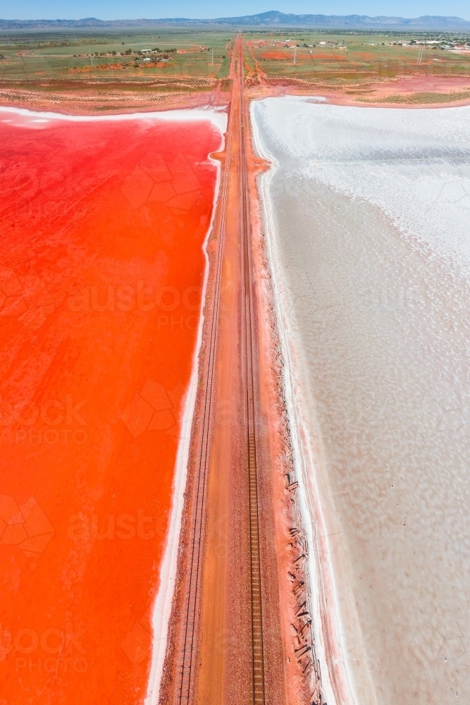 Aerial view of a railway line running across a salt lake with one side vivid red in colour - Australian Stock Image