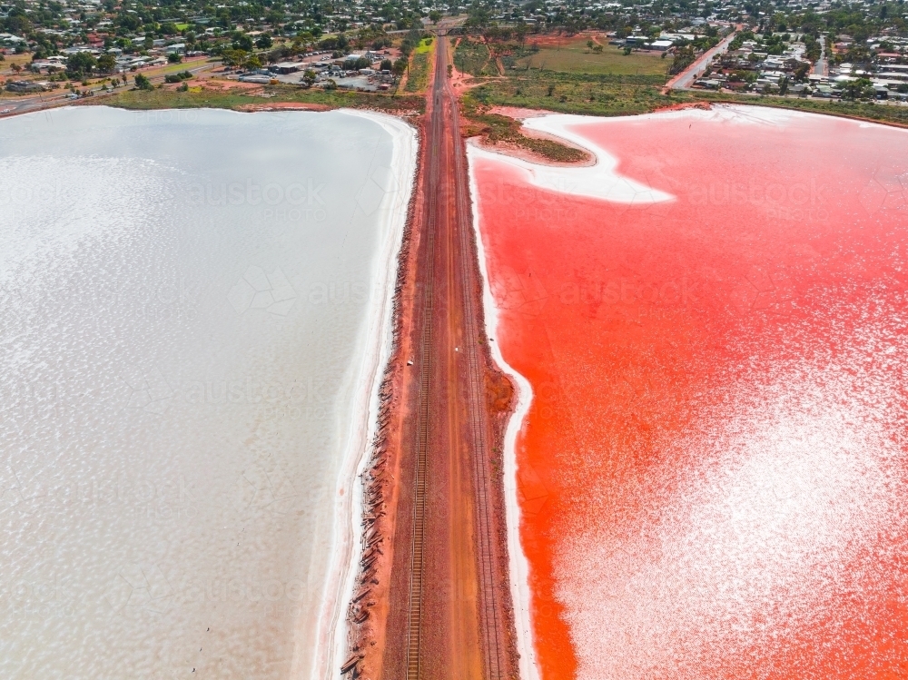 Aerial view of a railway line running across a salt lake with one side vivid red in colour - Australian Stock Image
