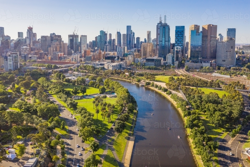 Aerial View of a river flowing through parkland toward a city skyline - Australian Stock Image
