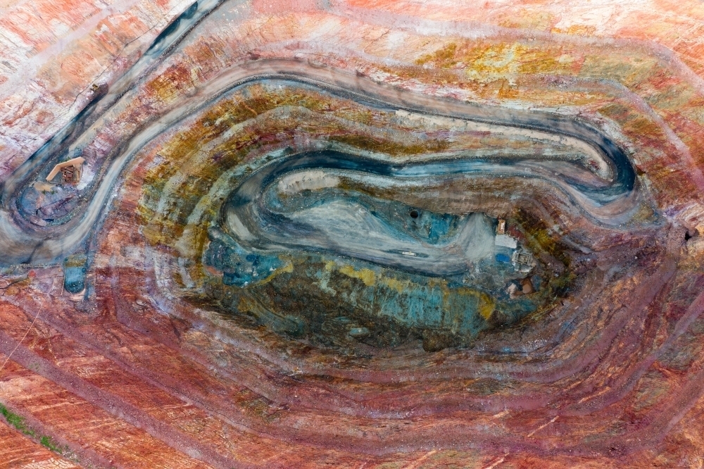 Aerial view of a road winding down into a large open cut mine with various colours of earth - Australian Stock Image