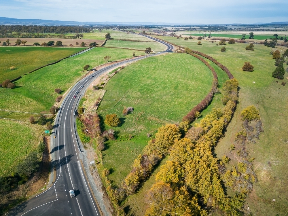 Aerial view of a road winding through green farmland into the distance - Australian Stock Image