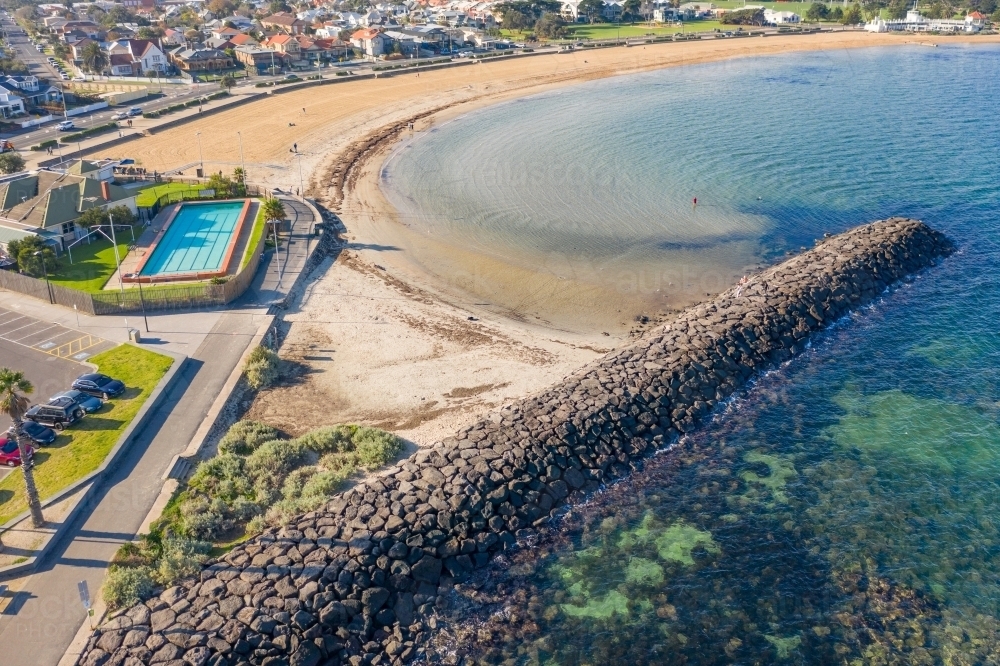 Aerial view of a rock breakwater jutting out next to a beach - Australian Stock Image