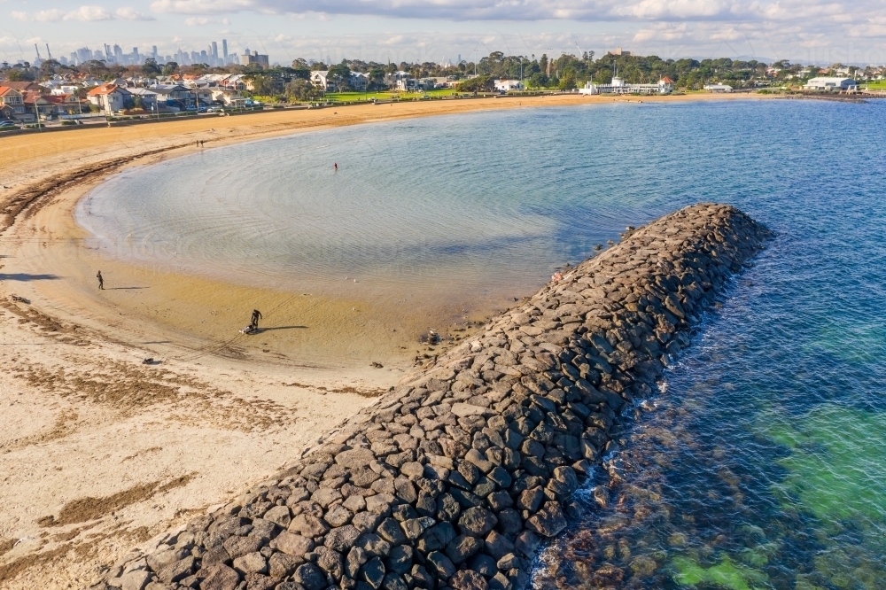 Aerial view of a rock breakwater jutting out next to a beach - Australian Stock Image