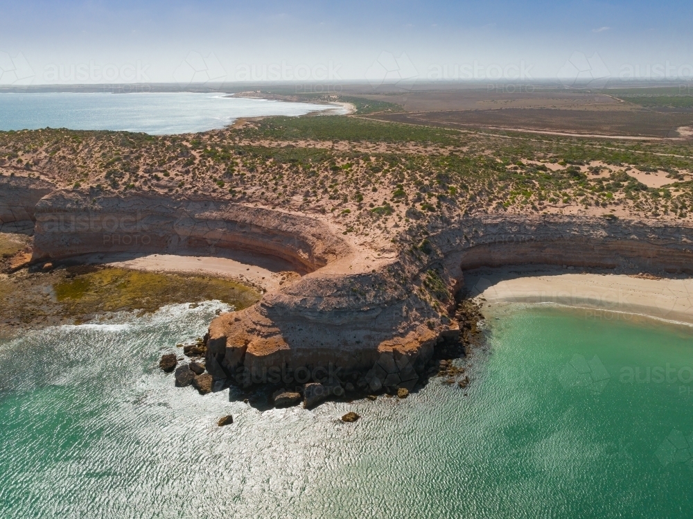 Aerial view of a rocky coastal headland protruding into a calm bay with cliffs and beaches alongside - Australian Stock Image