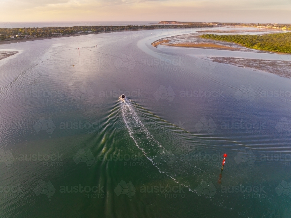 Aerial view of a small boat creating a wake in a wide coastal river - Australian Stock Image
