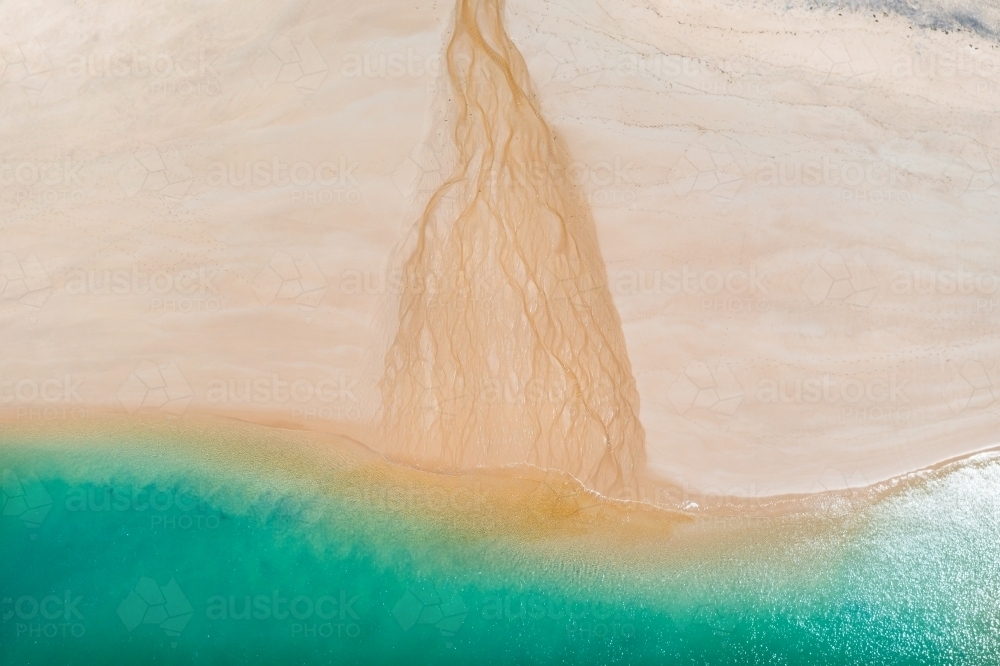 Aerial view of a small creek flowing over a white sandy beach into the sea - Australian Stock Image