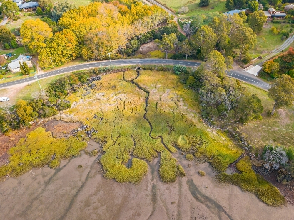 Aerial view of a small creek winding through marshland and under a curve in the road. - Australian Stock Image